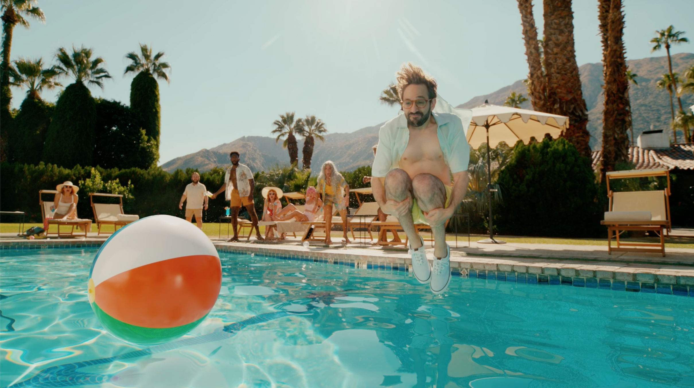 A man leaps into a pool with a large inflatable ball floating on the surface