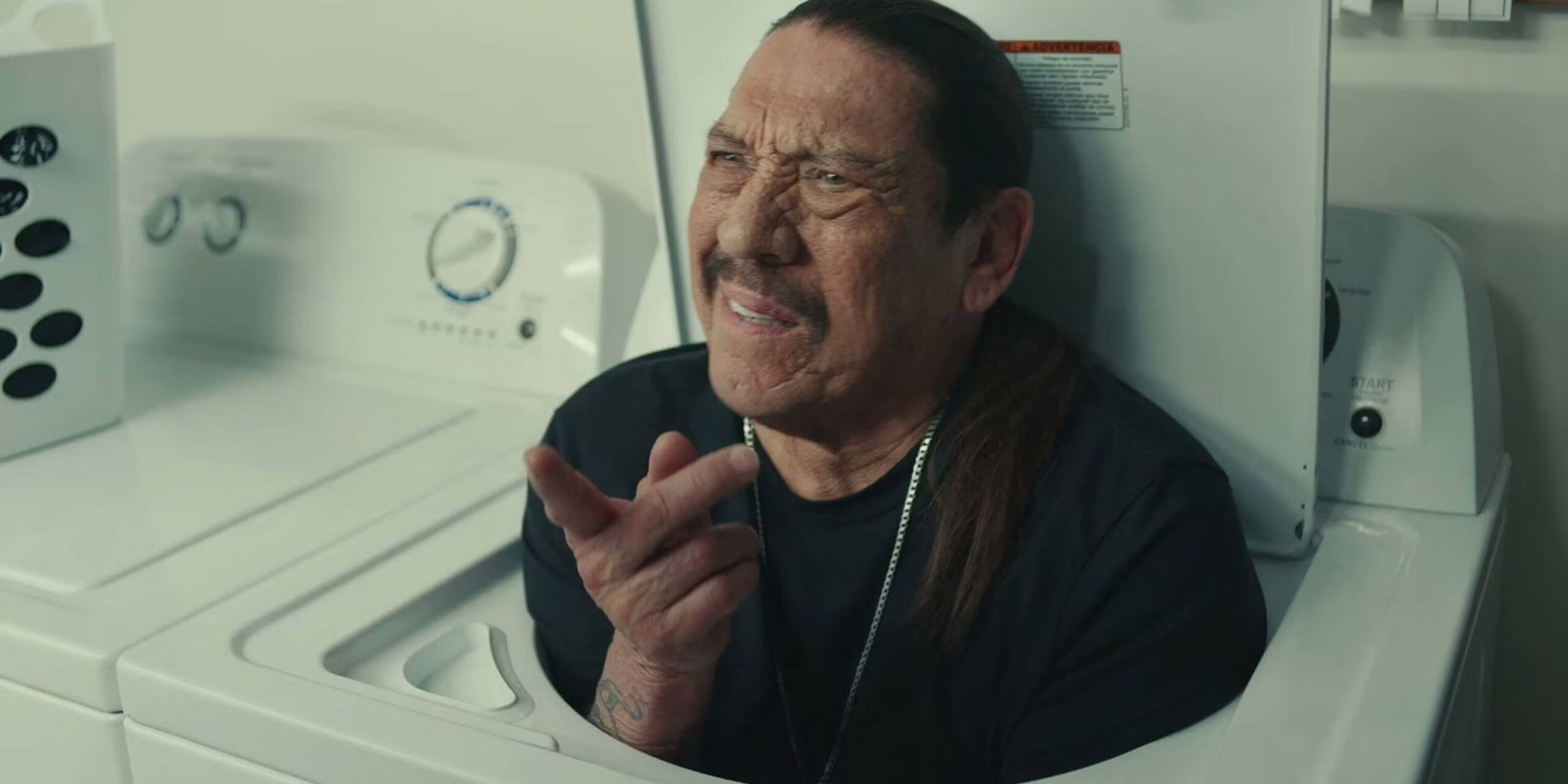 Actor Danny Trejo sticking out of a washing machine, pointing with an incredulous look on his face