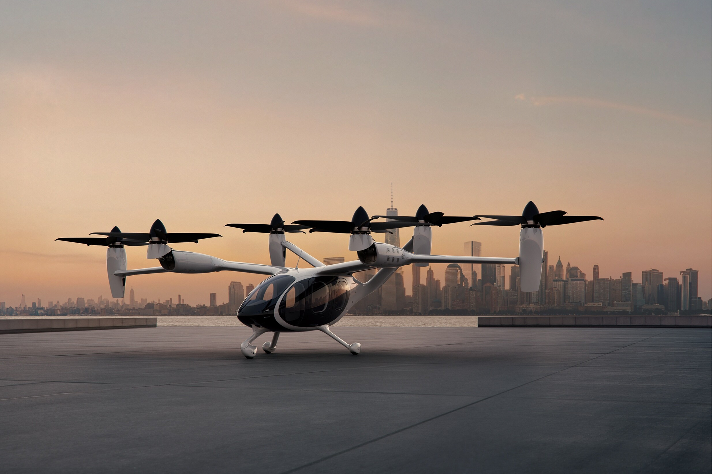The Joby aircraft parked on a large concrete landing pad with a city skyline in the background