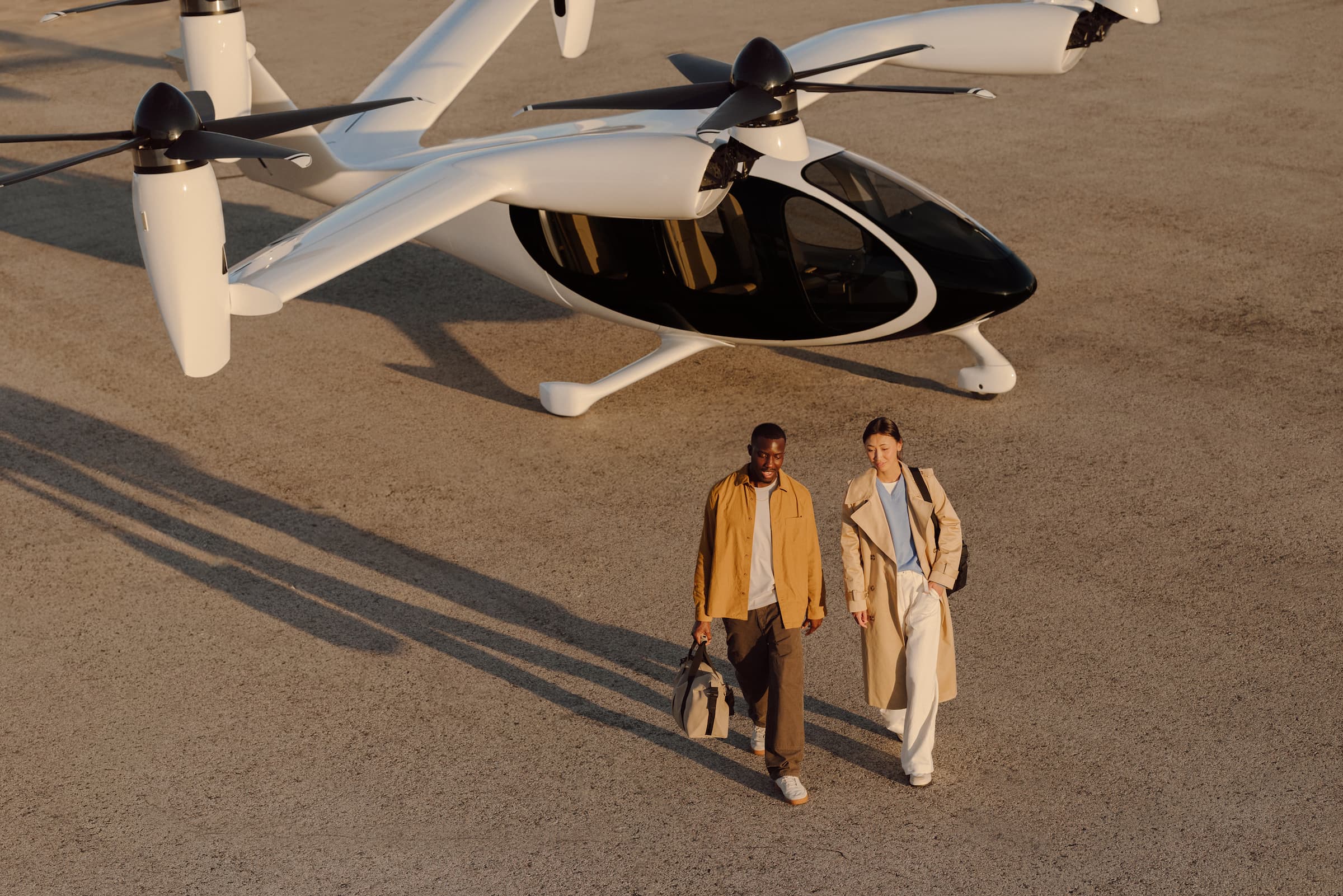 A man and woman walk away from the Joby aircraft on a tarmac, their shadows long behind them