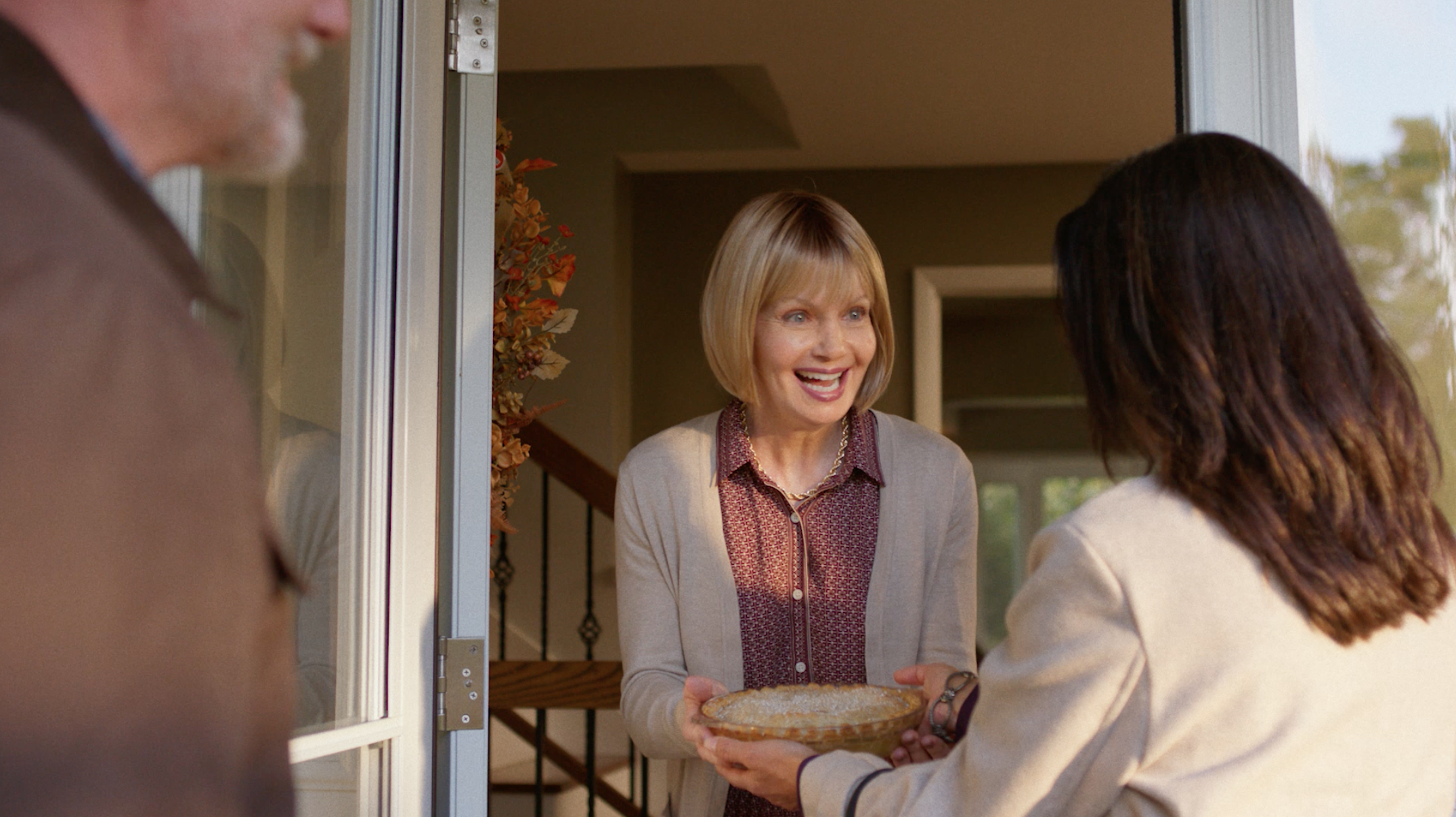 A woman greets another woman in the doorway of her home