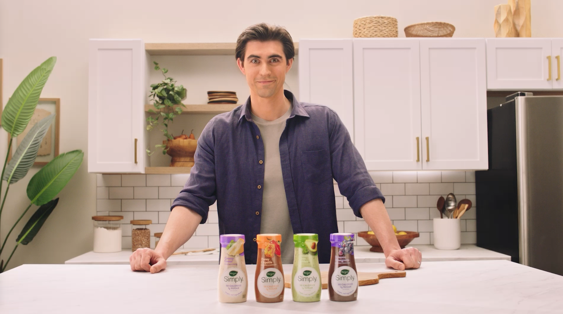 A man standing behind a counter with four types of Simply salad dressing.